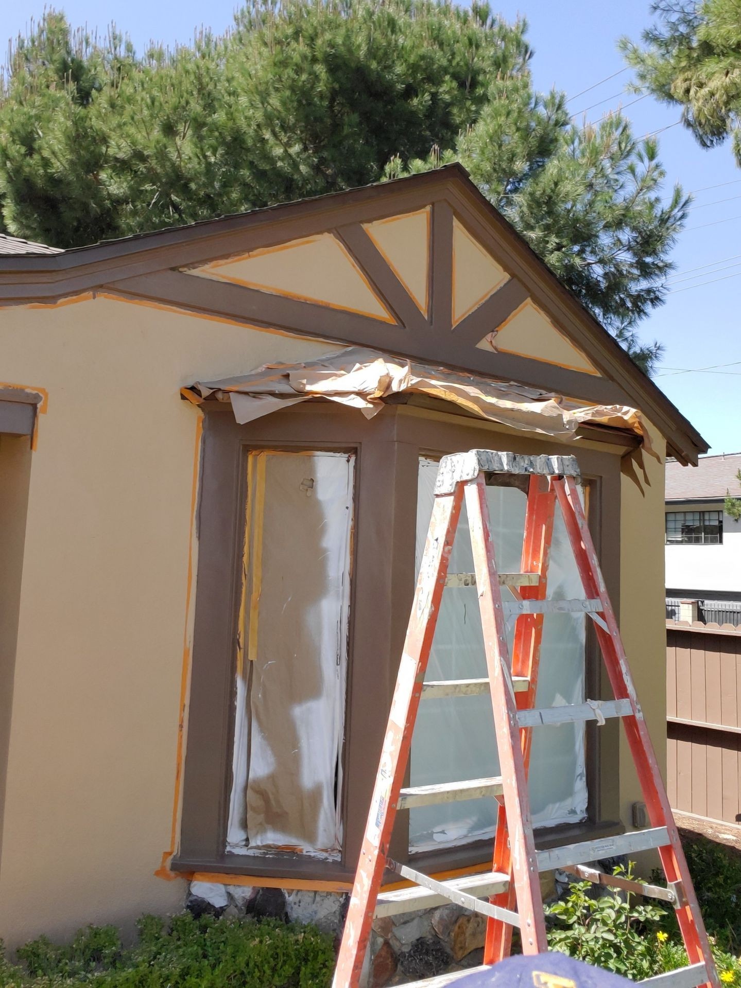 House being painted with a ladder in front and paper covering the windows and trim.