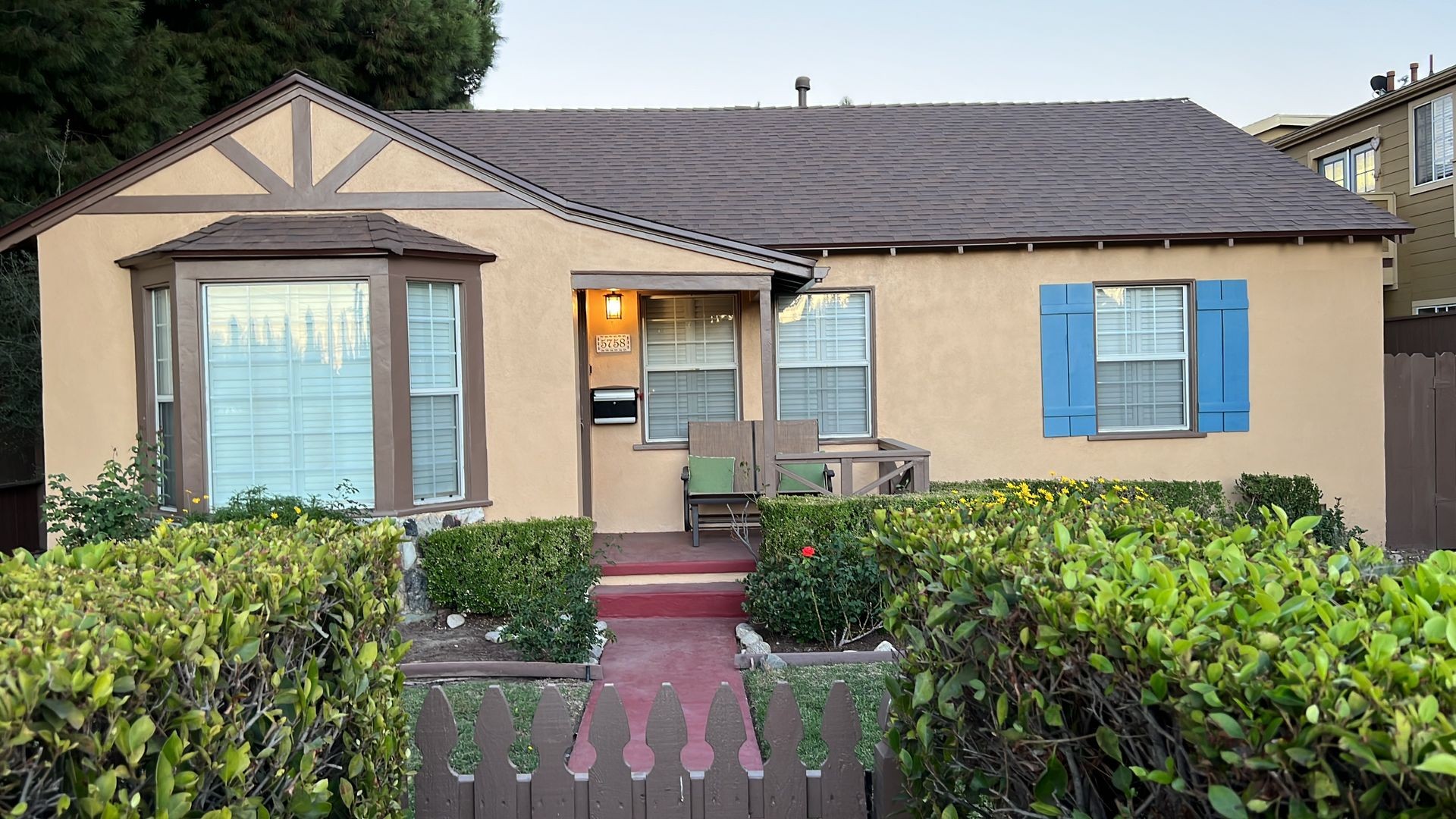 Small beige house with blue shutters, front porch, and manicured garden.